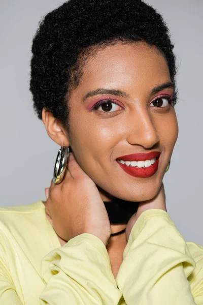 Despreocupado mujer afroamericana con maquillaje tocando cuello aislado en gris - foto de stock