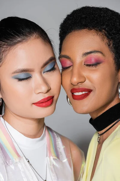 Retrato de mujer afroamericana despreocupada con labios rojos de pie cerca de un amigo asiático sobre fondo gris - foto de stock