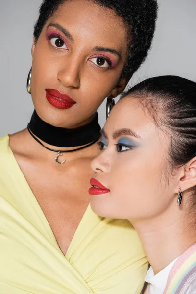 Portrait of short haired african american woman looking at camera near asian friend with red lips isolated on grey — Stock Photo