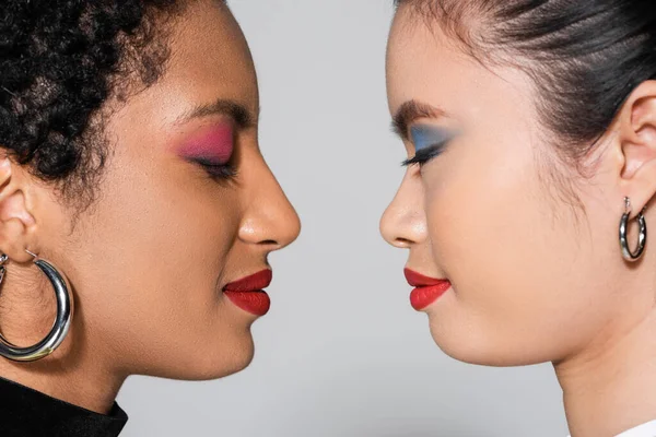 Side view of multiethnic models with bright makeup and closed eyes isolated on grey — Stock Photo