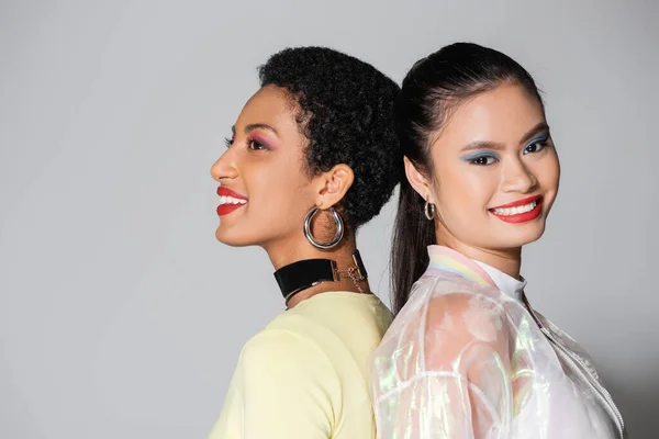 Pretty smiling interracial models with red lips standing back to back on grey background — Stock Photo