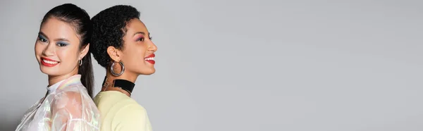 Positive asiatische Frau mit roten Lippen, Rücken an Rücken mit einem afrikanisch-amerikanischen Freund auf grauem Hintergrund, Banner — Stockfoto