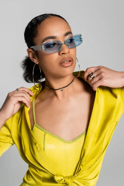 Гарна афроамериканська жінка в блакитних сонцезахисних окулярах і сережках кільця позує ізольовано на сірому — стокове фото