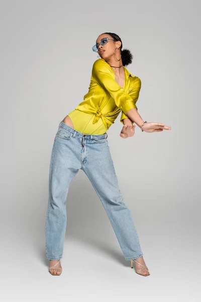 Comprimento total de mulher americana africana encantadora em jeans e camisa da moda posando em cinza — Fotografia de Stock