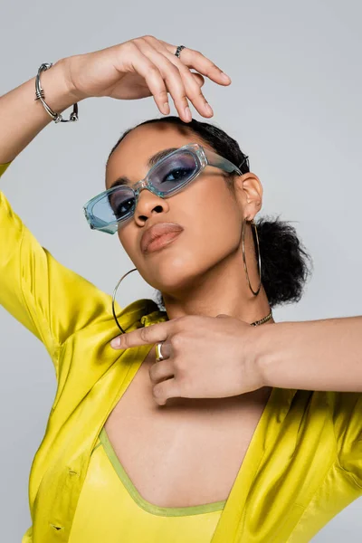 Красива афроамериканська жінка в блакитних сонцезахисних окулярах і стильний жест одягу ізольована на сірому — стокове фото
