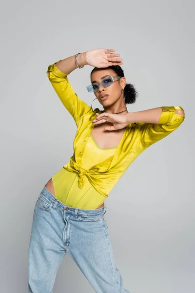 Pretty african american woman in blue sunglasses and stylish shirt gesturing isolated on grey — Stock Photo