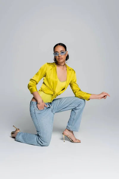 Повна довжина молодої афроамериканської моделі, що стоїть на коліні, позує з рукою в кишені на сірому — стокове фото
