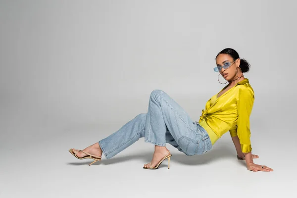 Volle Länge der stilvollen afrikanisch-amerikanische Frau in High Heels und trendige Sonnenbrille posiert auf grauem Hintergrund — Stockfoto