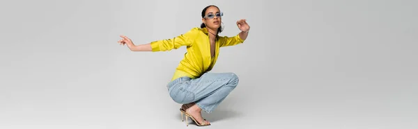 Stilvolles afrikanisch-amerikanisches Model in High Heels und trendigem Outfit, sitzend auf grauen Haxen, Banner — Stockfoto