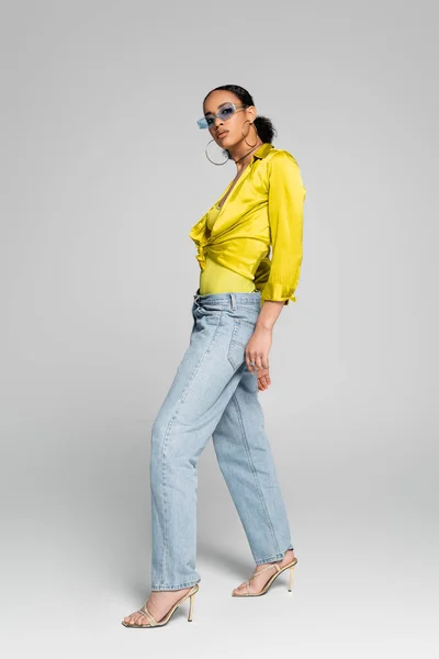 Full length of stylish african american model in trendy sunglasses and high heels posing on grey — Stock Photo