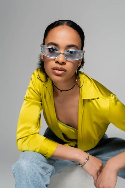 Ritratto di giovane modello afroamericano in eleganti occhiali da sole guardando la fotocamera isolata sul grigio — Foto stock