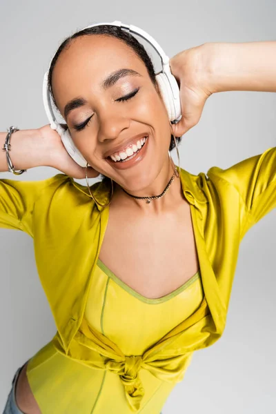 Happy african american woman listening music in wireless headphones isolated on grey — Stock Photo
