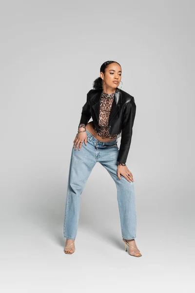 Full length of stylish african american model in cropped jacket and jeans posing on grey — Stock Photo