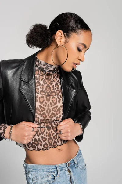 Fashionable african american woman in black cropped jacket adjusting turtleneck with animal print isolated on grey — Stock Photo