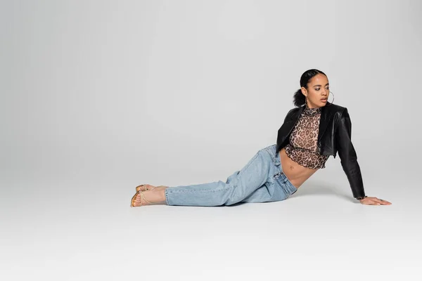 Volle Länge der stilvollen afrikanisch-amerikanische Frau in High Heels und trendiges Outfit sitzt auf grauem Hintergrund — Stockfoto