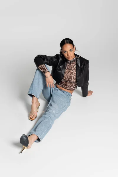 Hochwinkelaufnahme eines afrikanisch-amerikanischen Models in hochhackigen Sandalen und trendigem Outfit auf grau sitzend — Stockfoto