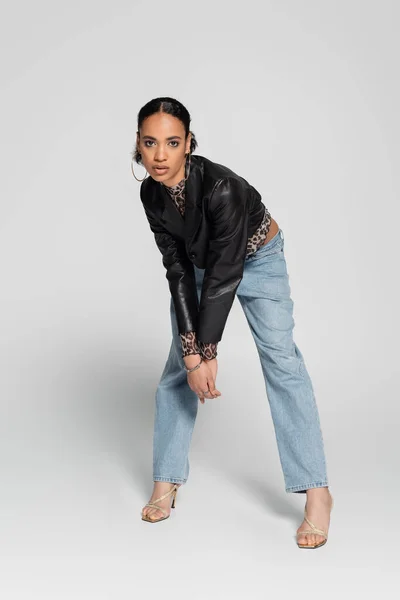Volle Länge der modischen afrikanisch-amerikanische Frau in trendigen abgeschnittenen Jacke und hochhackigen Sandalen Blick in die Kamera auf grau — Stockfoto