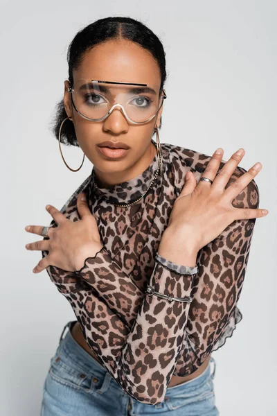 Stylish african american woman in crop top with animal print and trendy sunglasses posing with crossed arms isolated on grey — Stock Photo
