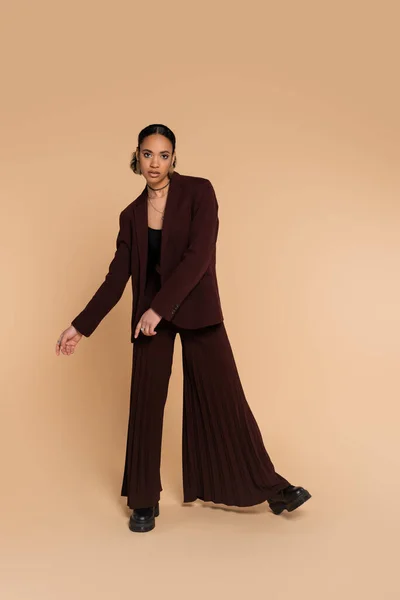 Full length of young african american woman in stylish suit with wide pants posing on beige — Stock Photo