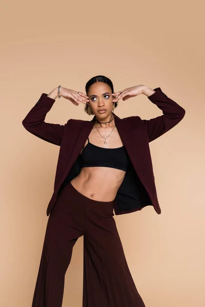 Young african american woman in crop top and stylish maroon blazer posing isolated on beige — Stock Photo
