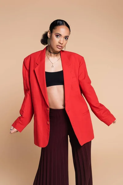 Elegante modelo afro-americano em top de cultura e blazer vermelho posando isolado no bege — Fotografia de Stock