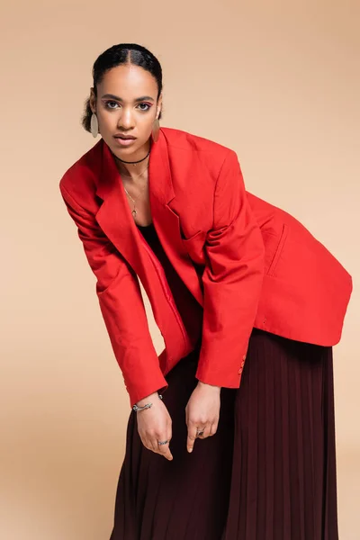 Young african american woman in maroon wide pants and bright red blazer posing isolated on beige — Stock Photo