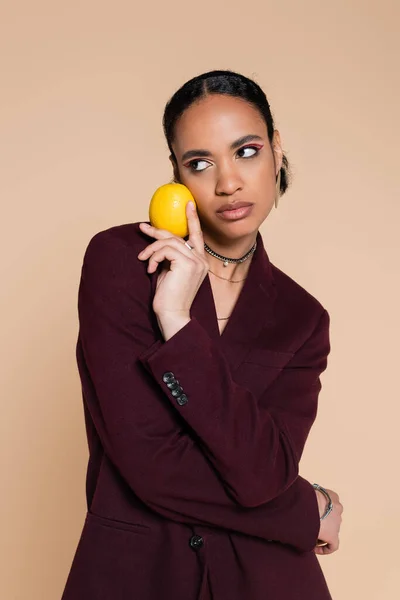 Afrikanisch-amerikanisches Model in weinrotem Blazer posiert mit reifer Zitrone isoliert auf beige — Stockfoto