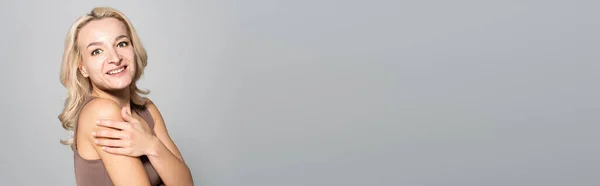 Donna bionda sorridente con acne spalla toccante isolata su grigio, banner — Foto stock