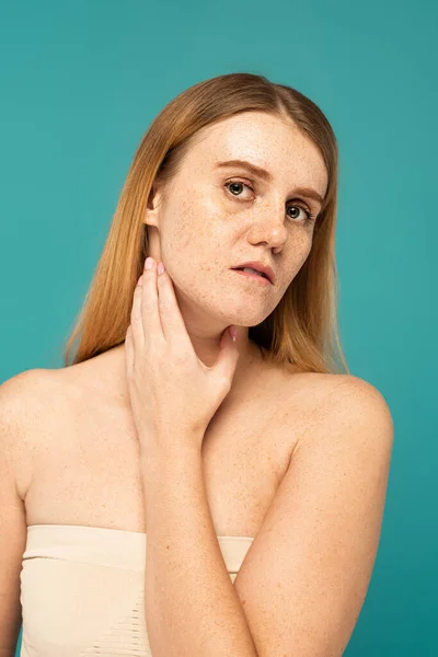 Молода жінка з плямистою шкірою торкається шиї ізольована на бірюзовому — стокове фото