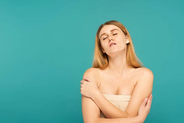 Junge Frau mit sommersprossiger Haut berührt nackte Schultern isoliert auf Türkis — Stockfoto