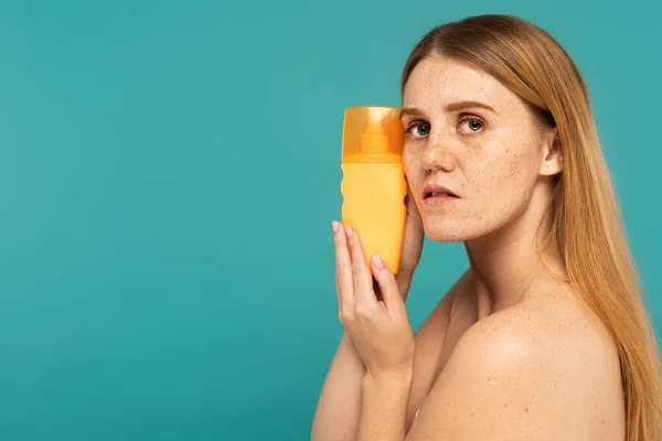 Молода жінка з веснянками на шкірі тримає сонцезахисний крем ізольовано на бірюзовому — стокове фото