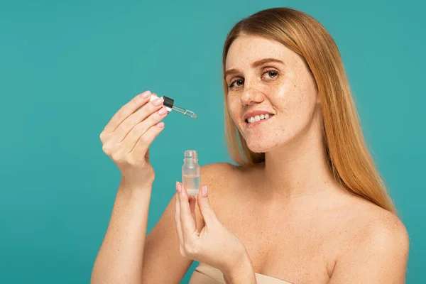 Smiling woman with freckled skin holding serum and dropper isolated on turquoise — Stock Photo