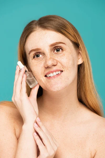 Carefree woman with freckles holding serum isolated on turquoise — Stock Photo