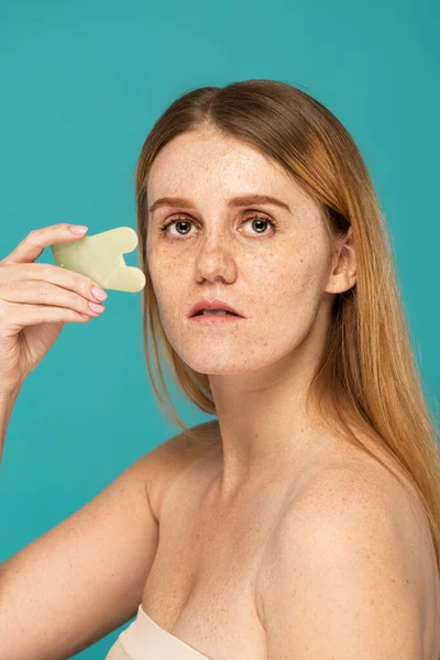 Jeune femme avec des taches de rousseur en utilisant grattoir visage isolé sur turquoise — Photo de stock