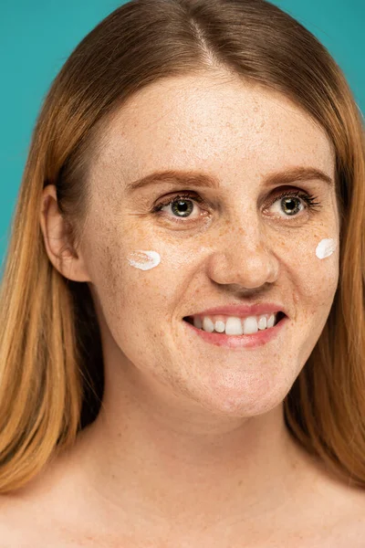 Closed up of happy woman with freckles and cream on face isolated on turquoise — Stock Photo