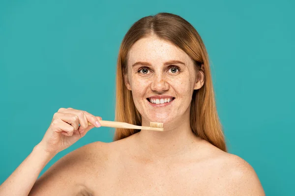 Donna lentigginosa con i capelli rossi sorridente mentre tiene lo spazzolino isolato sul turchese — Foto stock
