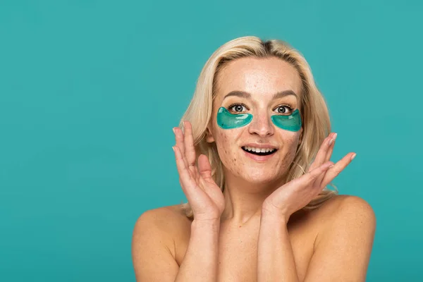 Amazed woman with acne and moisturizing eye patches smiling isolated on turquoise — Stock Photo