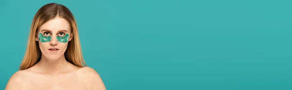 Rousse femme avec des taches de rousseur et des taches de rousseur sous les yeux regardant la caméra isolée sur turquoise, bannière — Photo de stock