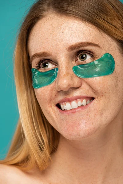 Portrait of happy woman with freckles and collagen patches under eyes smiling isolated on turquoise — Stock Photo