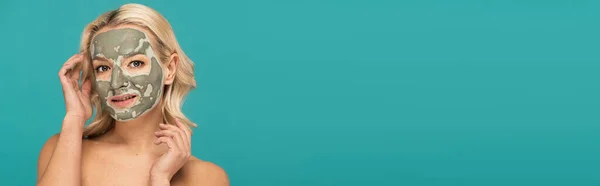 Blonde woman with face mask looking at camera isolated on turquoise, banner — Stock Photo