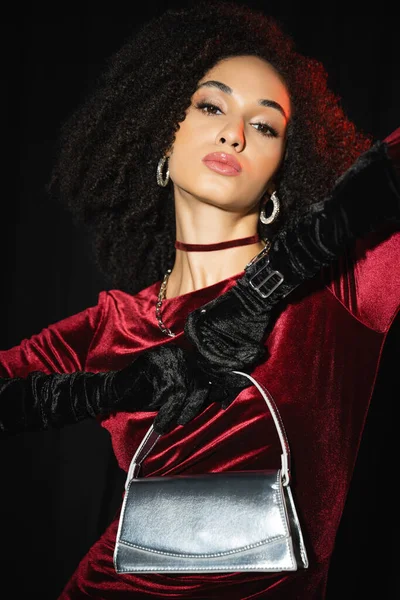 Portrait of african american woman in velvet dress and gloves holding handbag isolated on black — Stock Photo