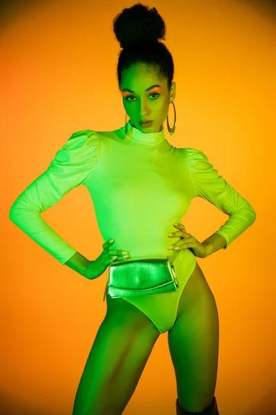 Stylish african american model in neon bodysuit with waist bag on orange background — Stock Photo