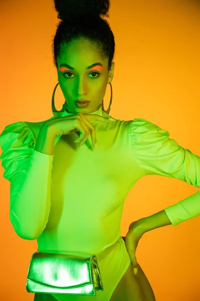 Trendy african american woman in neon bodysuit with waist bag standing isolated on orange — Stock Photo