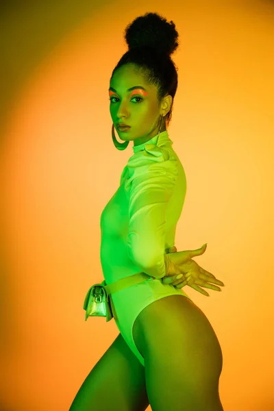 Sexy afrikanisch-amerikanisches Model im neonfarbenen Body schaut in die Kamera auf orangefarbenem Hintergrund — Stockfoto
