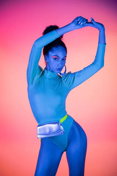 Modisches afrikanisch-amerikanisches Model mit Neon-Visage und Body, der Hände auf hellrosa Hintergrund berührt — Stockfoto