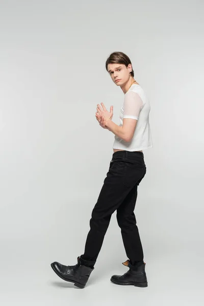Повна довжина модної великої моделі в чорних штанях і білій футболці, дивлячись на камеру на сірому фоні — стокове фото