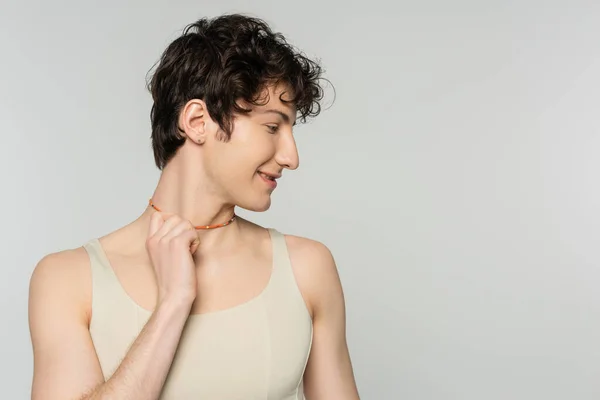 Profile of curly bigender model in tank top touching colorful beads isolated on grey — Stock Photo