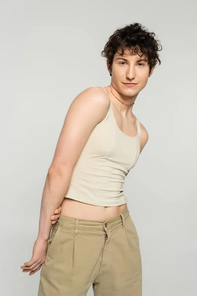 Modelo pansexual con estilo con cabello castaño ondulado mirando a la cámara aislada en gris - foto de stock