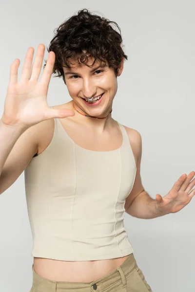 Carefree pangender person in tank top gesturing and smiling at camera isolated on grey — Stock Photo