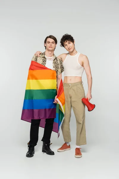 Full length of young nonbinary couple with lgbt flag and megaphone looking at camera on grey background — Stock Photo